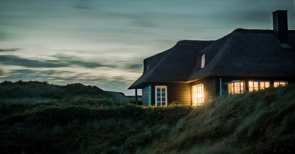 A scenic view of a cozy bungalow illuminated at dusk, nestled in lush greenery.