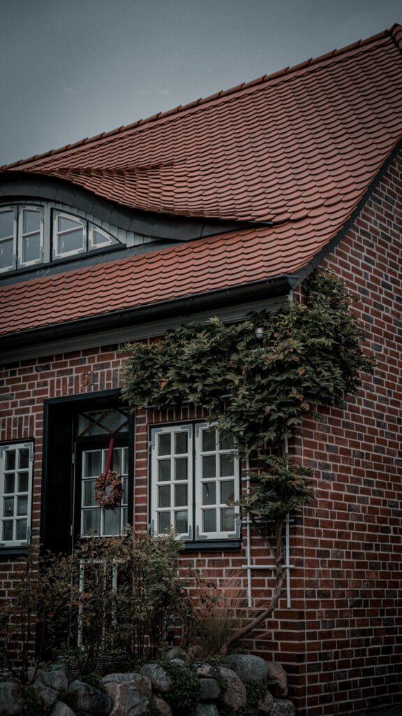 Cozy brick house with red roof and window plants, perfect for home inspiration.