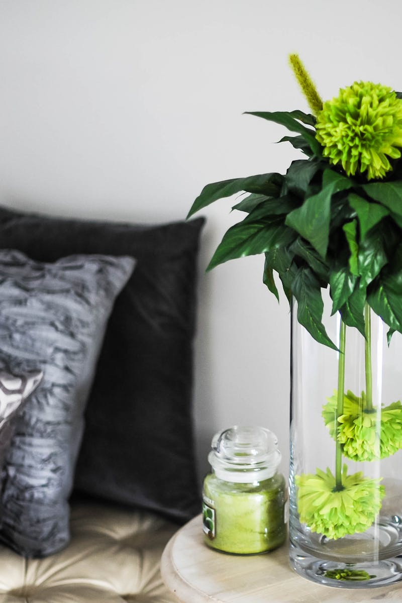 Sophisticated room decor featuring green flowers in a vase, soft pillows, and chic glass jar.